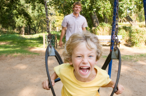 Screaming boy on swing with Dad in back