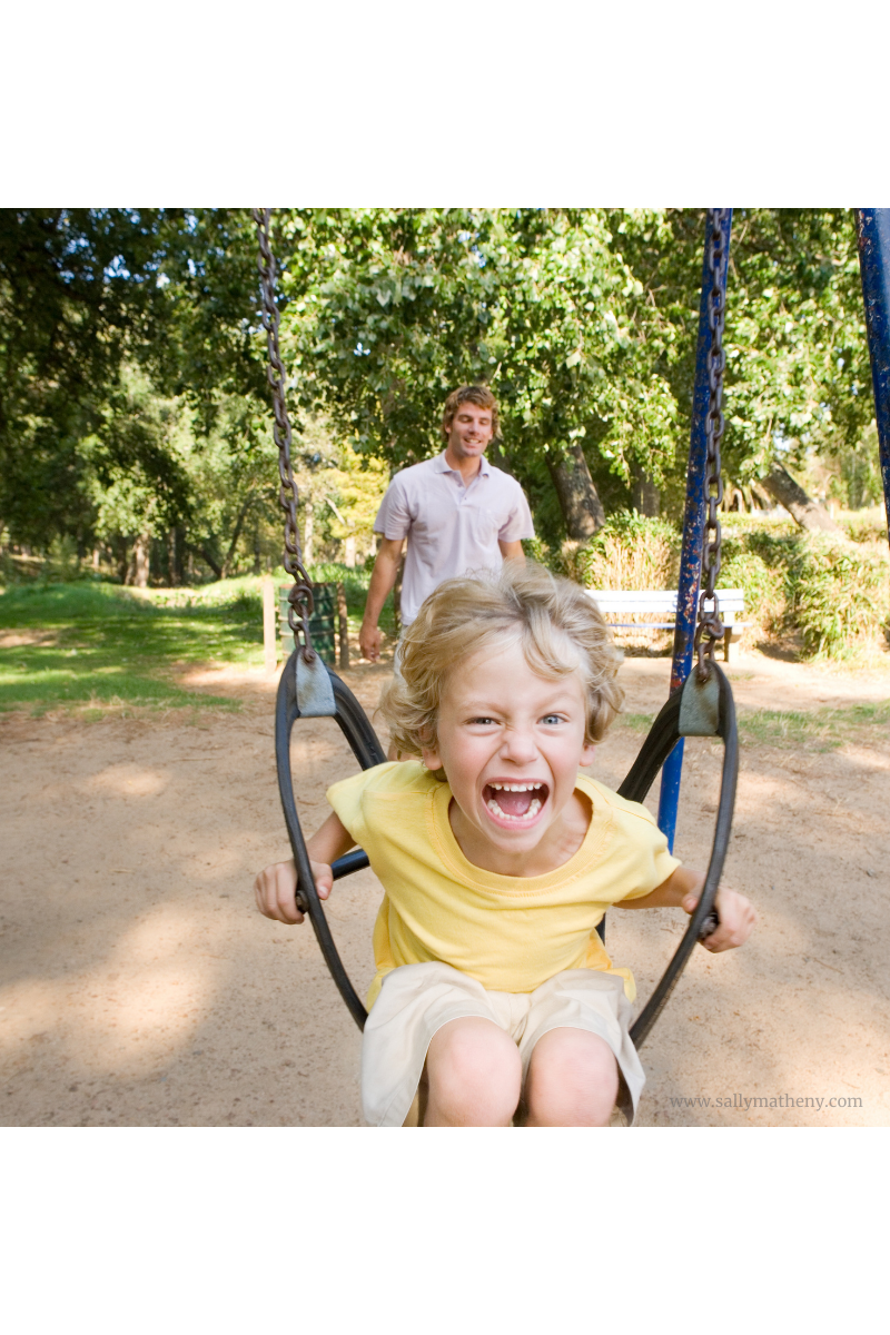 Screaming boy on swing with Dad in back