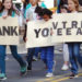 Children marching in parade holding thank you signs to veterans