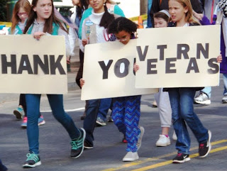 Children marching in parade holding thank you signs to veterans