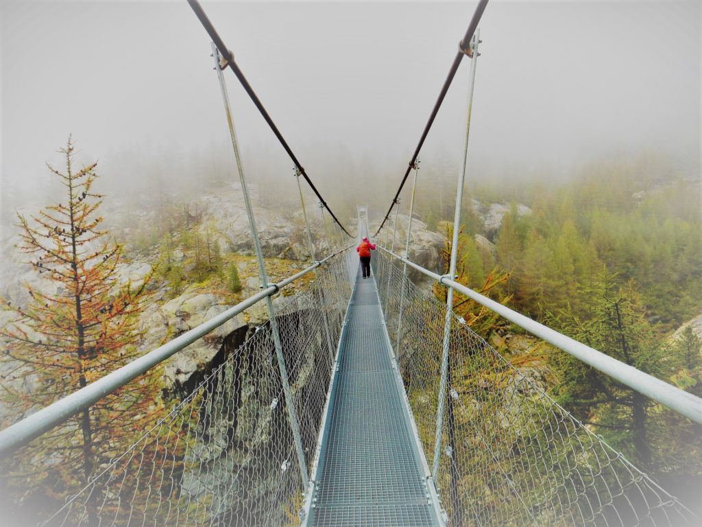 Person crossing a swinging bridge in the fog.