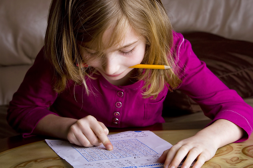 Young girl with pencil in her mouth working on math at home.