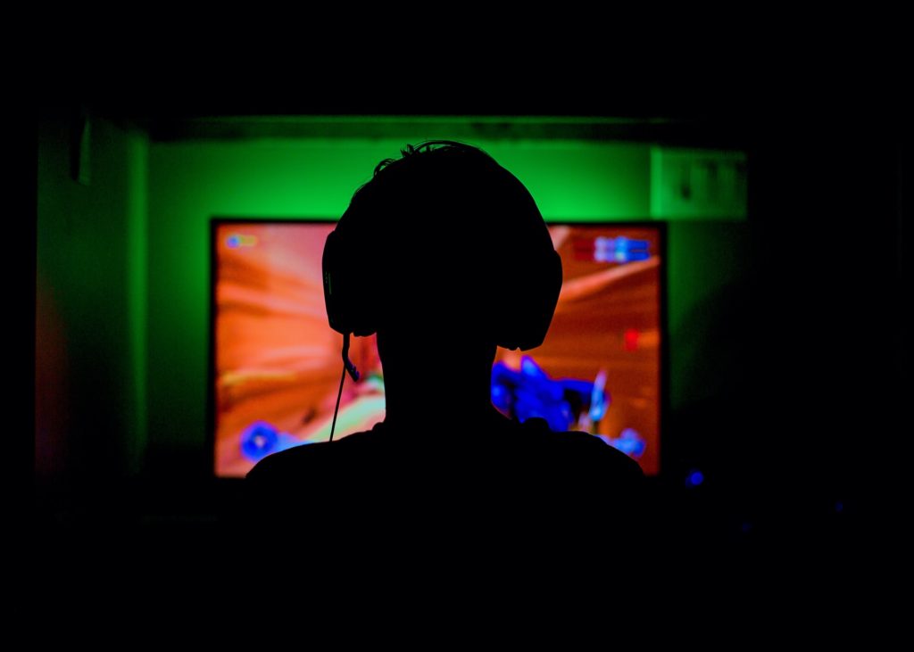 Teen sitting in front of gaming screen with headphones.