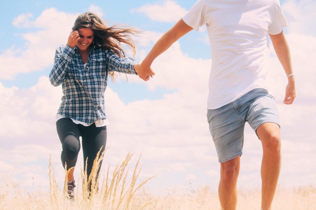 Husband leading smiling wife by hand in a field. 