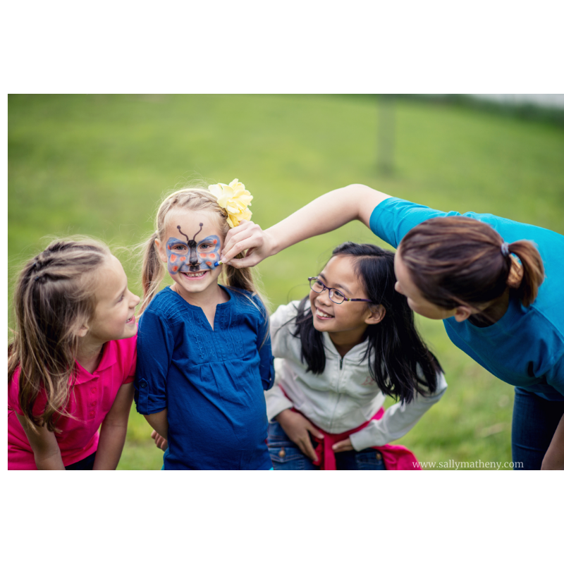 Teen face painting little girls' faces.