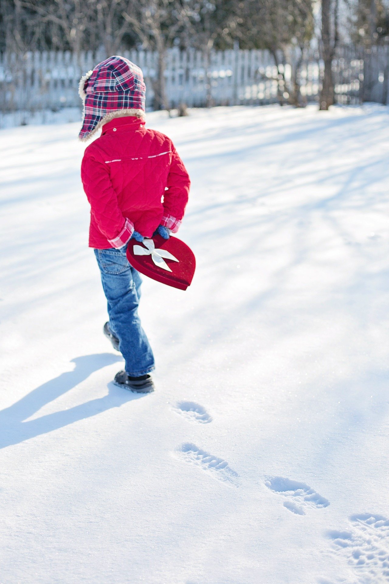 Child walking in snow and carrying a box of Valentine candy behind his/her back.