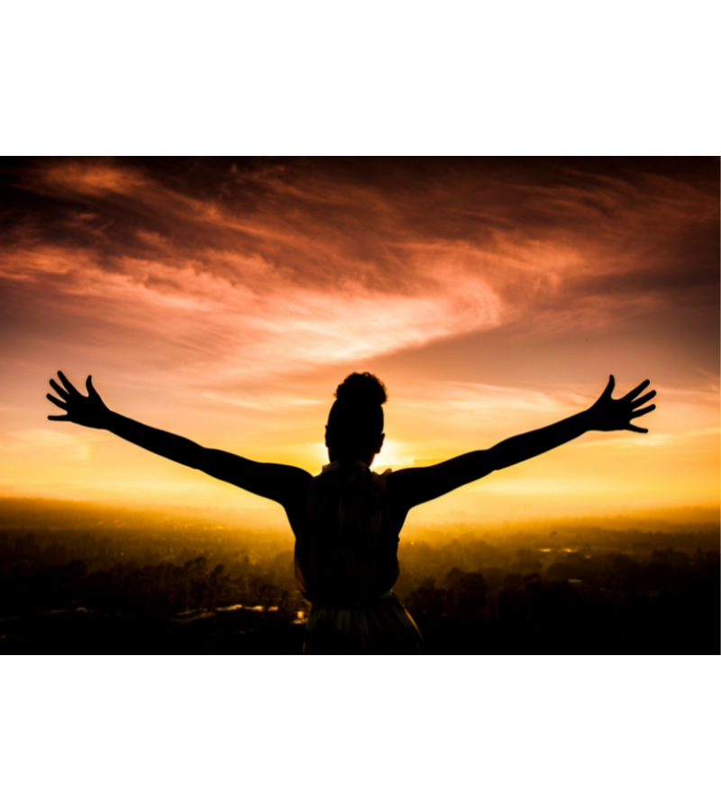 Woman raising hands praising God at sunset.