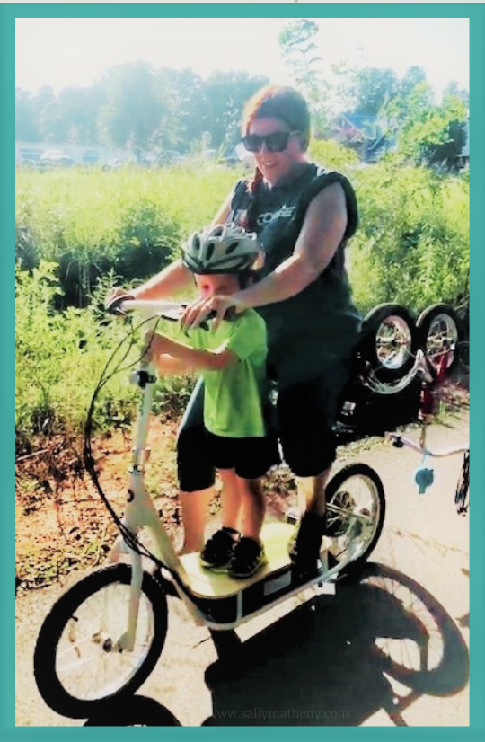 Sally on electric scooter with grandson. His tricycle is hanging off the back.
Matheny, 2020.