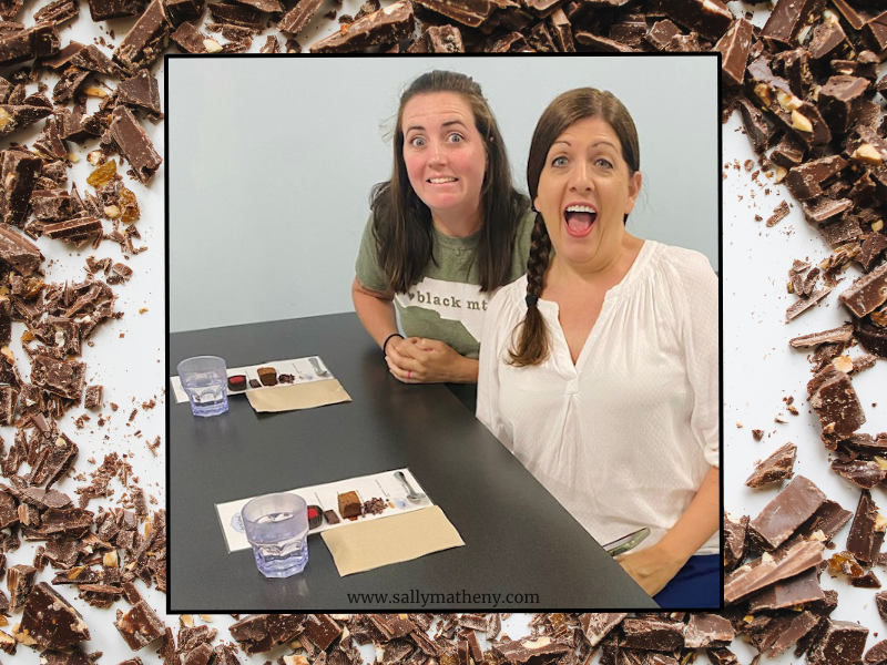 Shows a photo of Sally Matheny and one of her daughters making funny faces about having to wait before diving into the chocolates placed on a mat before them.